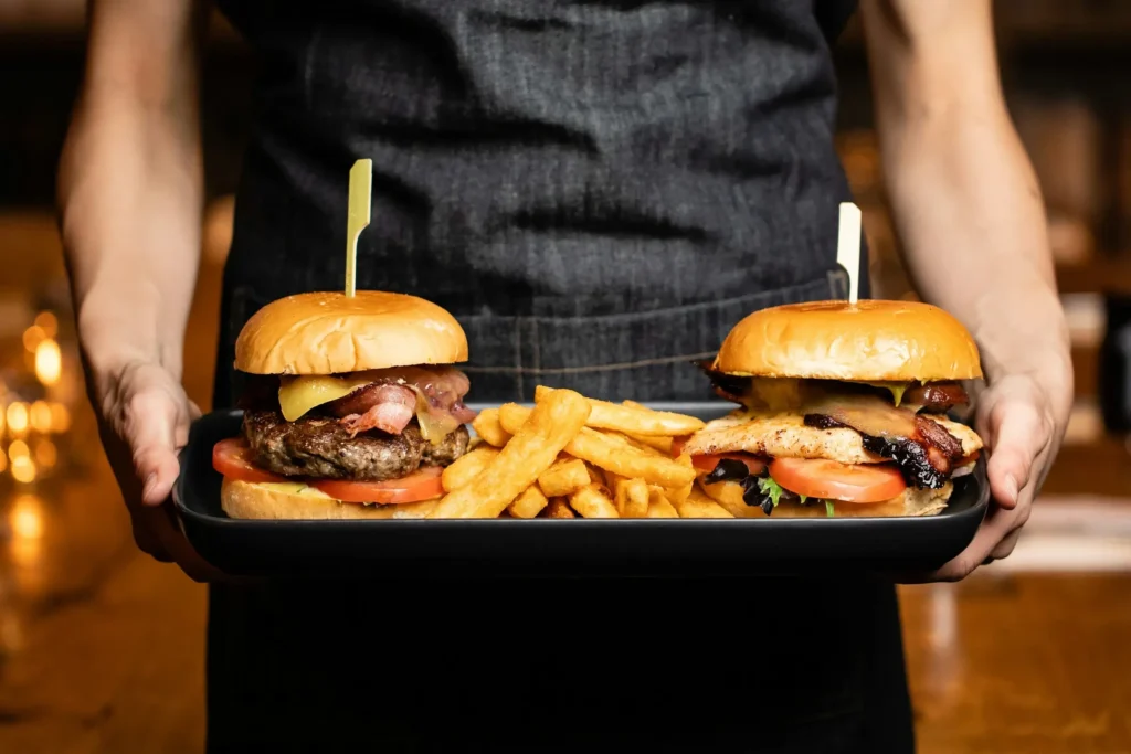 person holding burgers and chips on a plate