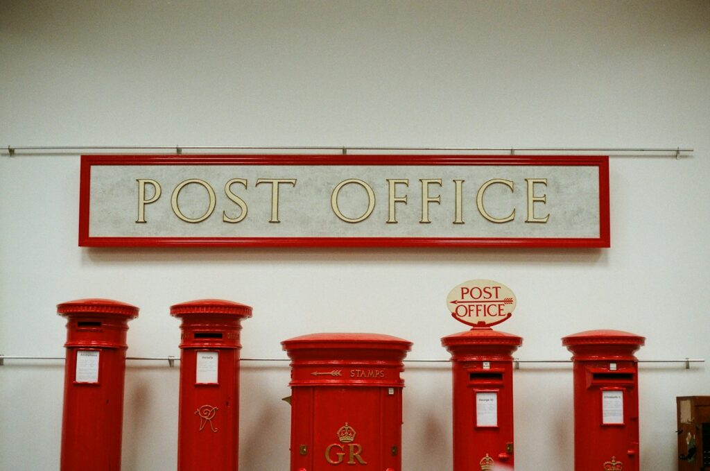 Five red post boxes under a post office sign